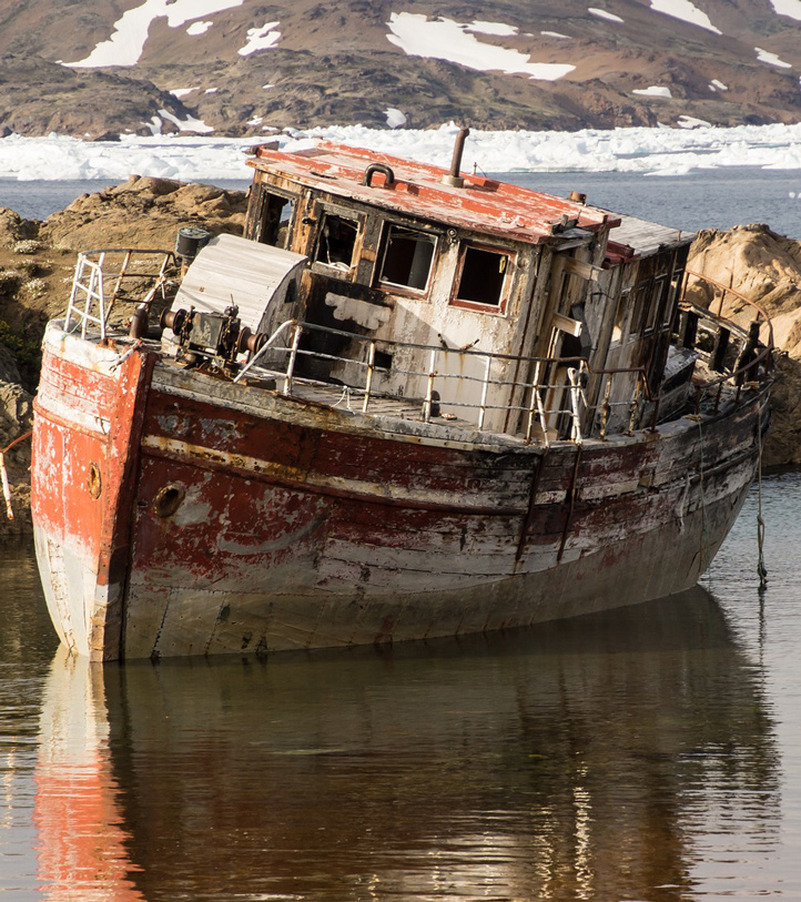 A rusty, old, ship with a cabin sitting in shallow water.